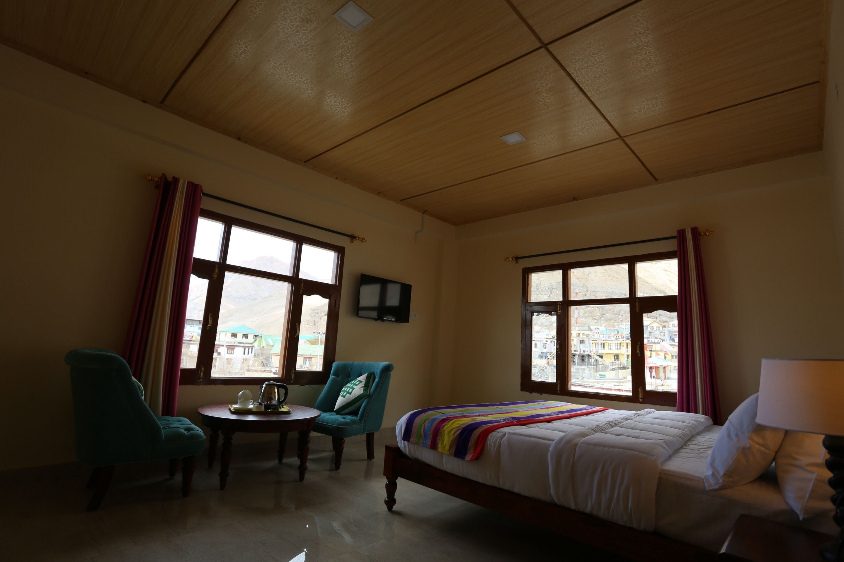 A hotel room with a bed, two chairs, a small table, and large windows offering a view of buildings outside.