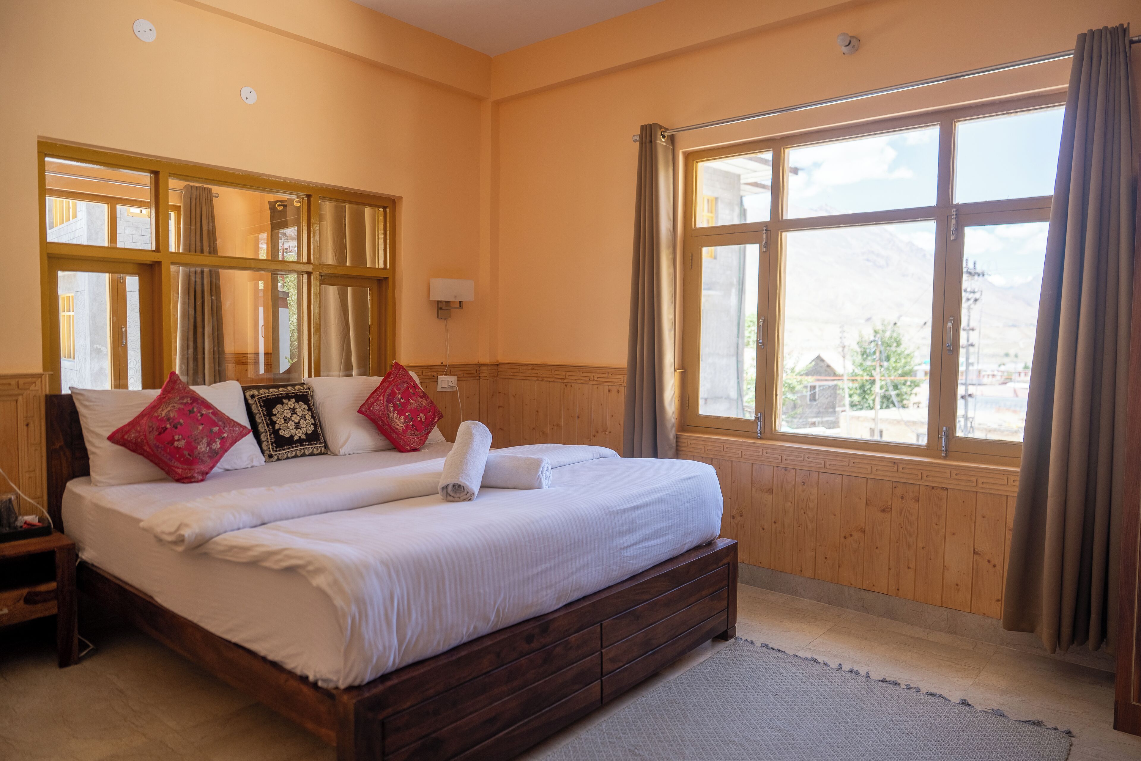 A bedroom with a large bed, wooden headboard, a window with curtains, and a view of the outside.