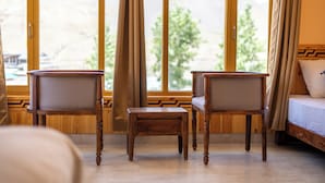 A room with a bed, two wooden chairs, a small table, and a large window with curtains. - Spiti Heritage (Spiti)