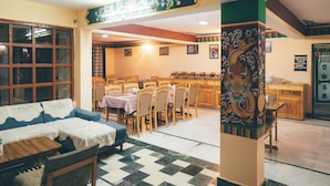 A dining area with wooden tables and chairs, a blue sofa, and a patterned floor. - Spiti Heritage (Spiti)