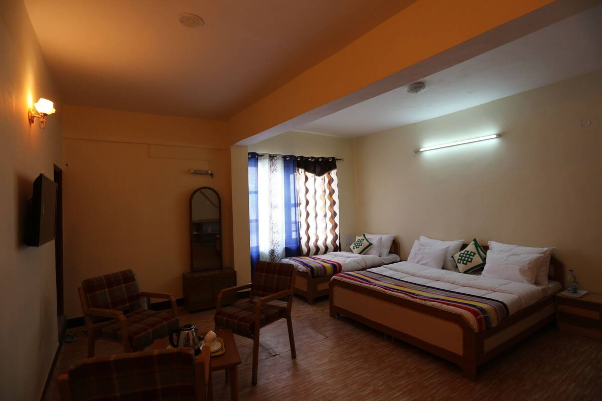 A hotel room with a bed, two chairs, a desk, a mirror, and a window with curtains.