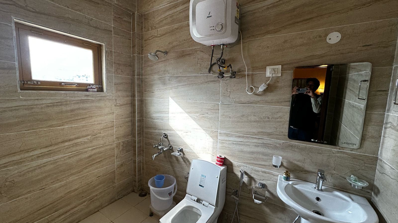 A bathroom with a toilet, sink, shower, and a window.