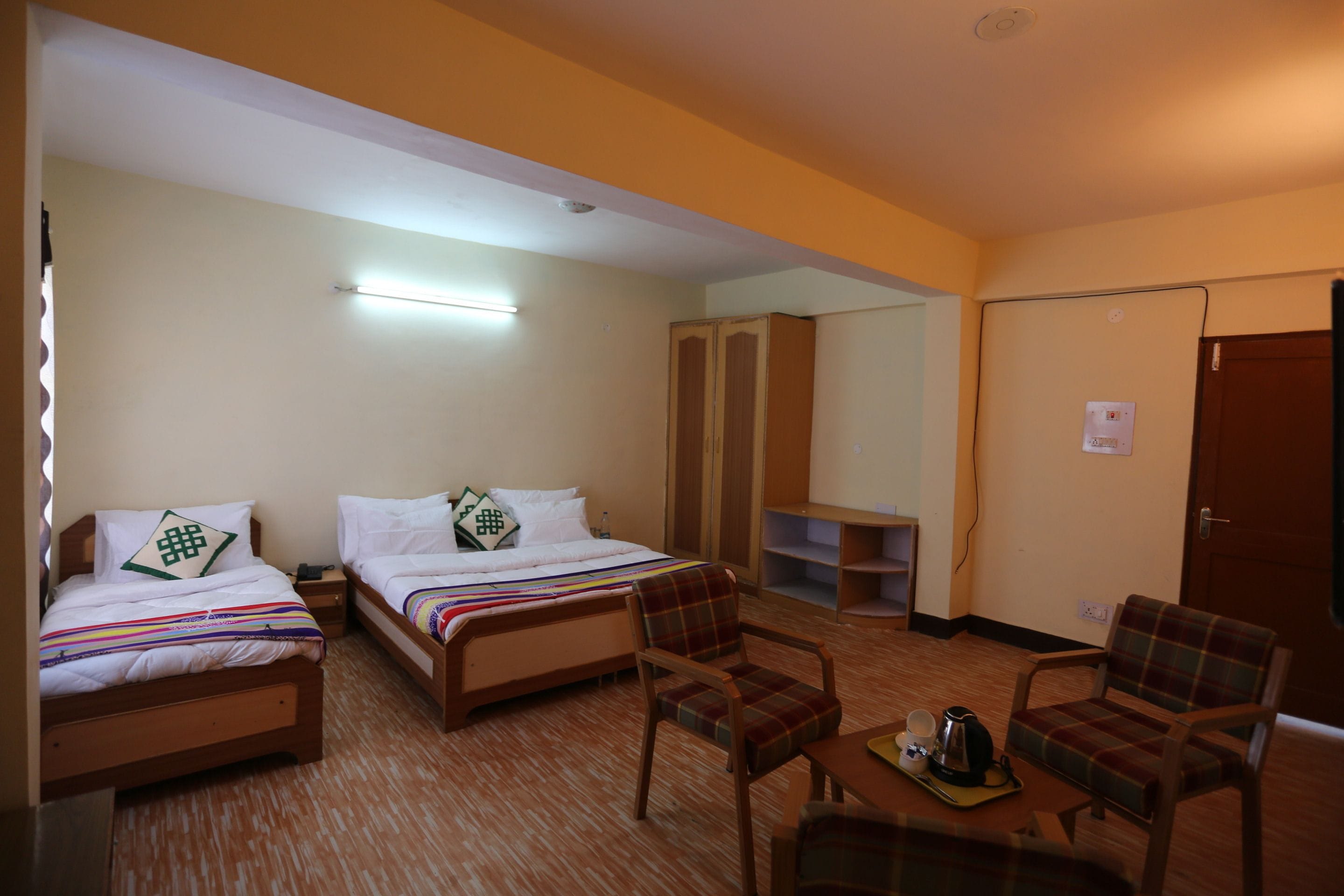 Quarto de hotel com duas camas, uma mesinha com chaleira e uma cadeira.