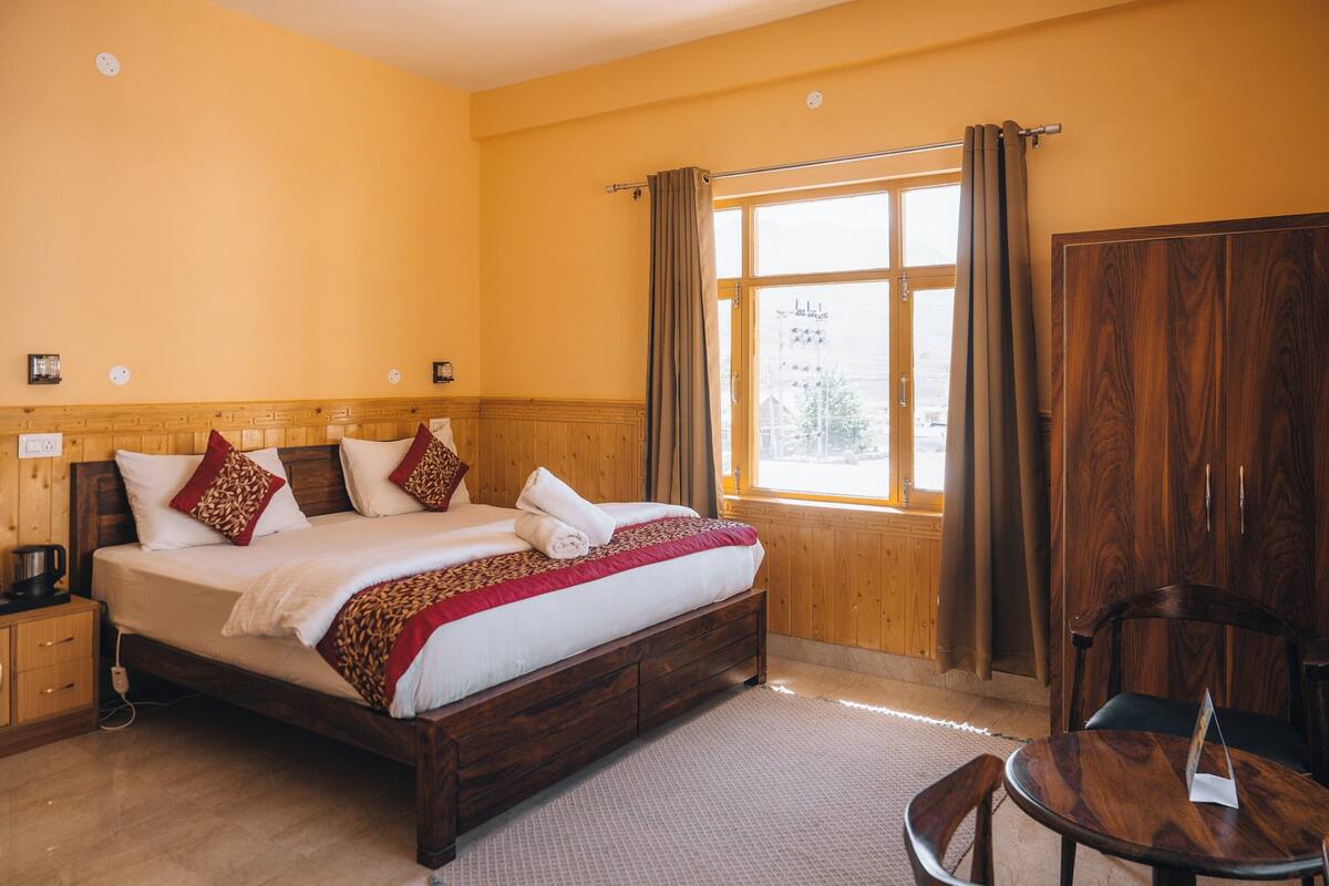 A hotel room with a wooden bed, a small table, and a wardrobe.
