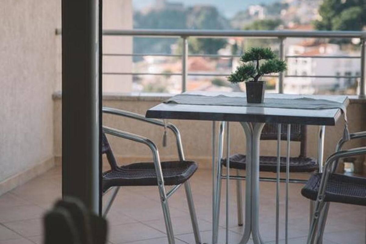 Un balcon avec une table et des chaises, un pot de fleurs et une vue sur la mer et les bâtiments.