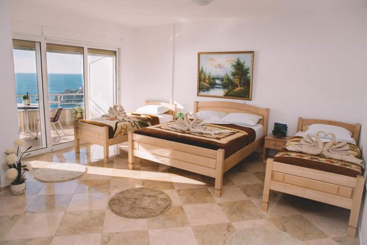 Une chambre d’hôtel avec deux lits en bois, un balcon donnant sur la mer et un tableau accroché au mur.