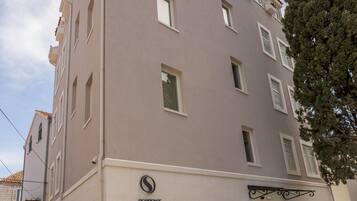 Un edificio residencial de varios pisos con fachada color beige, entrada protegida por un portón y un letrero que dice "Residence Stine".