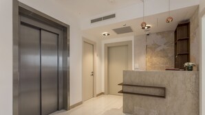 A modern reception area with a marble counter, a large metallic elevator, and a wooden shelving unit. - Residence Stine (Split)