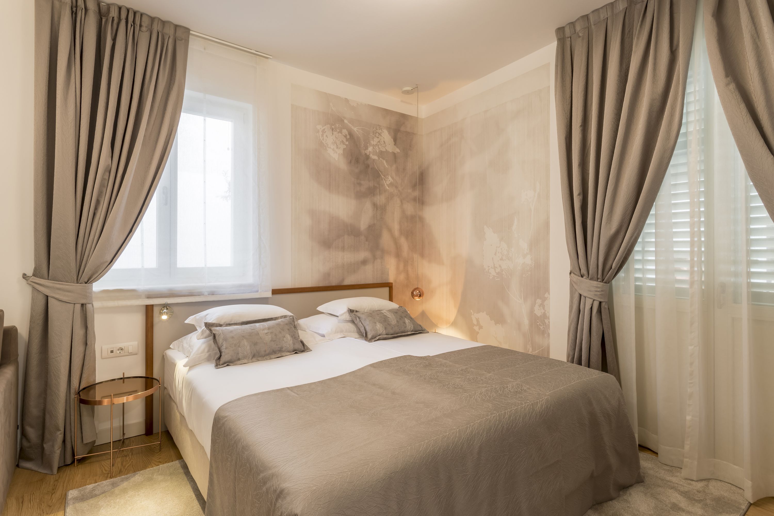 Un dormitorio con cama, cortinas, una mesita de noche y una pared con textura.