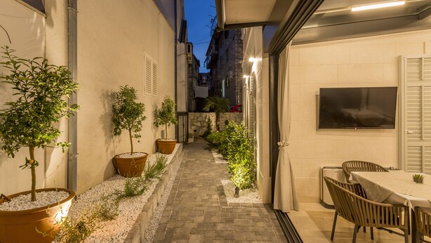 A narrow pathway flanked by potted plants leading to a covered outdoor seating area with a table and chairs. - Residence Stine (Split)
