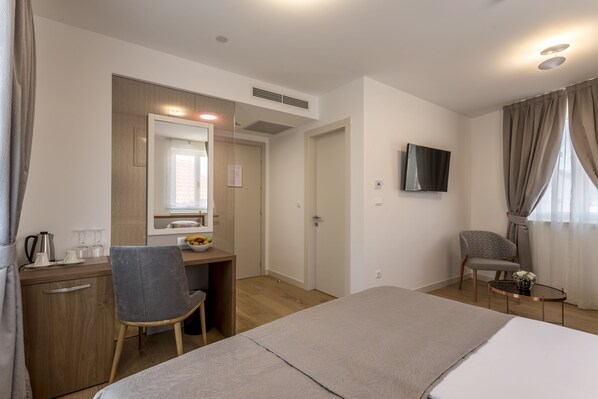 Una habitación de hotel con cama, escritorio con silla, televisor y una pequeña mesa con un florero.