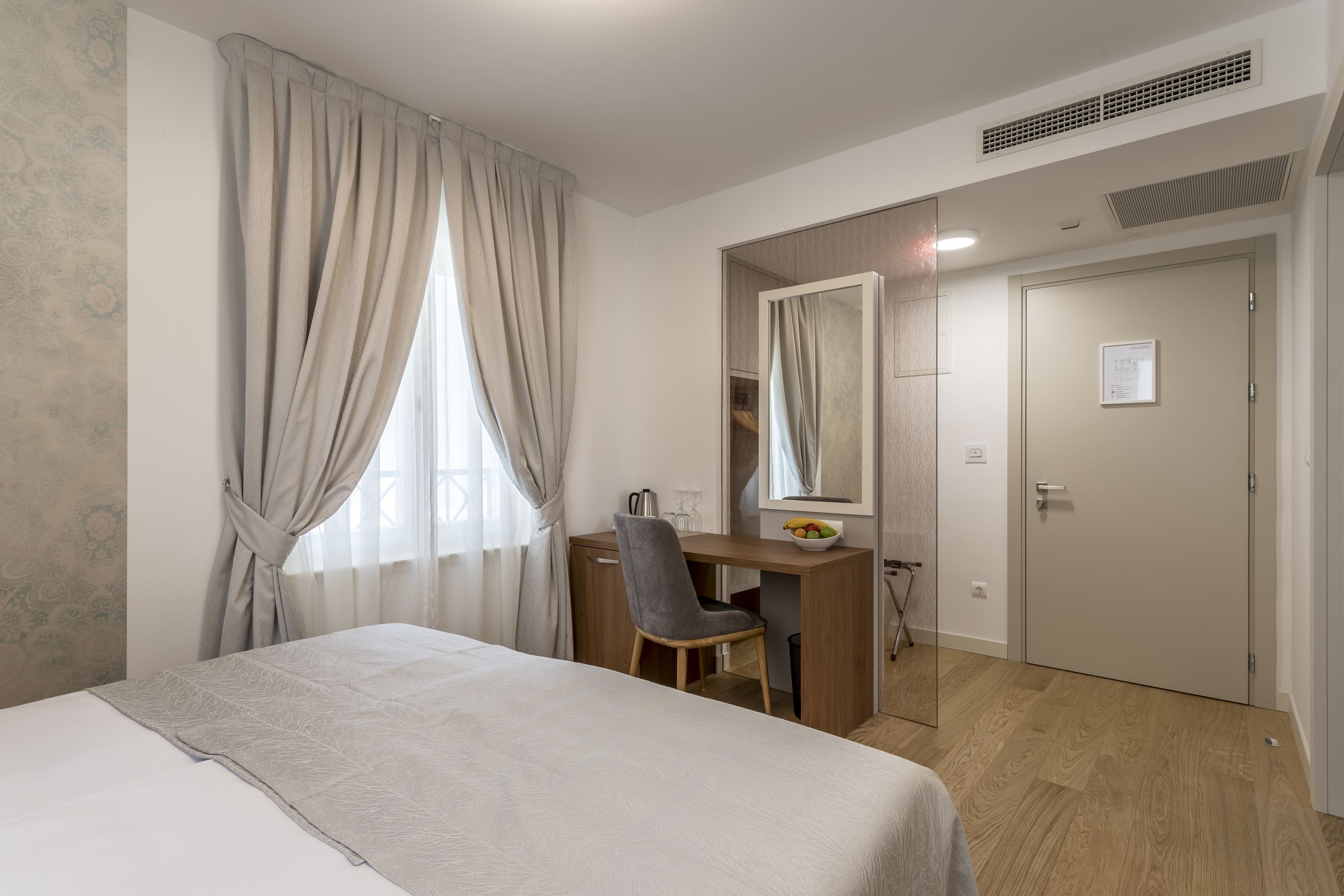 Una habitación de hotel con cama, escritorio, silla, espejo y puerta.