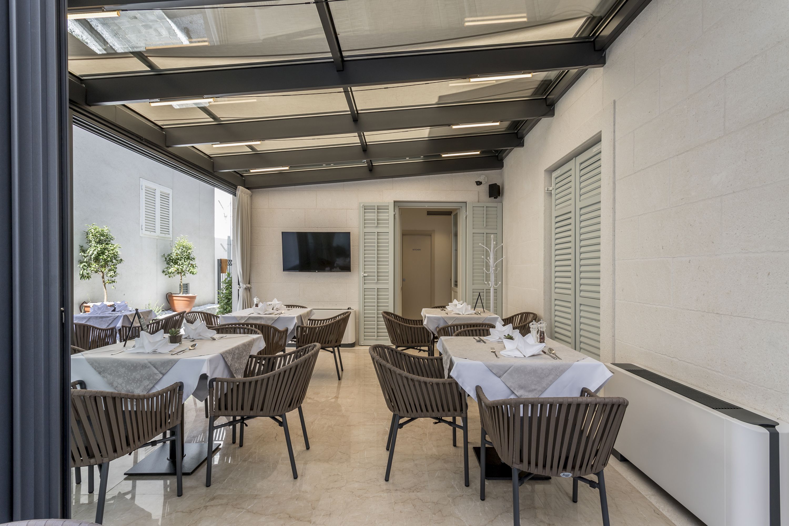 Un restaurante con mesas, sillas, una pantalla de televisión y plantas en macetas.