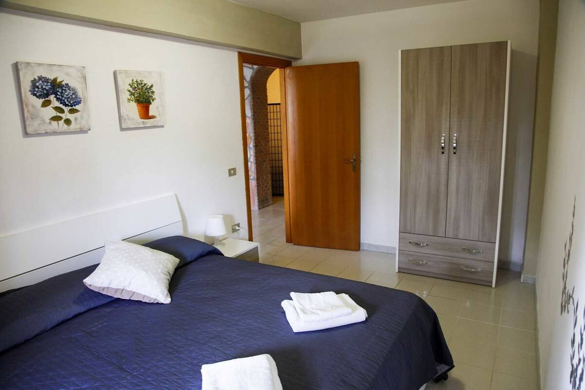 Une chambre à coucher avec un lit, deux tableaux accrochés au mur, une armoire et une porte de salle de bain.
