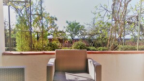Un balcón con mobiliario de mimbre, vista a un jardín con cerca de madera y cielo despejado.