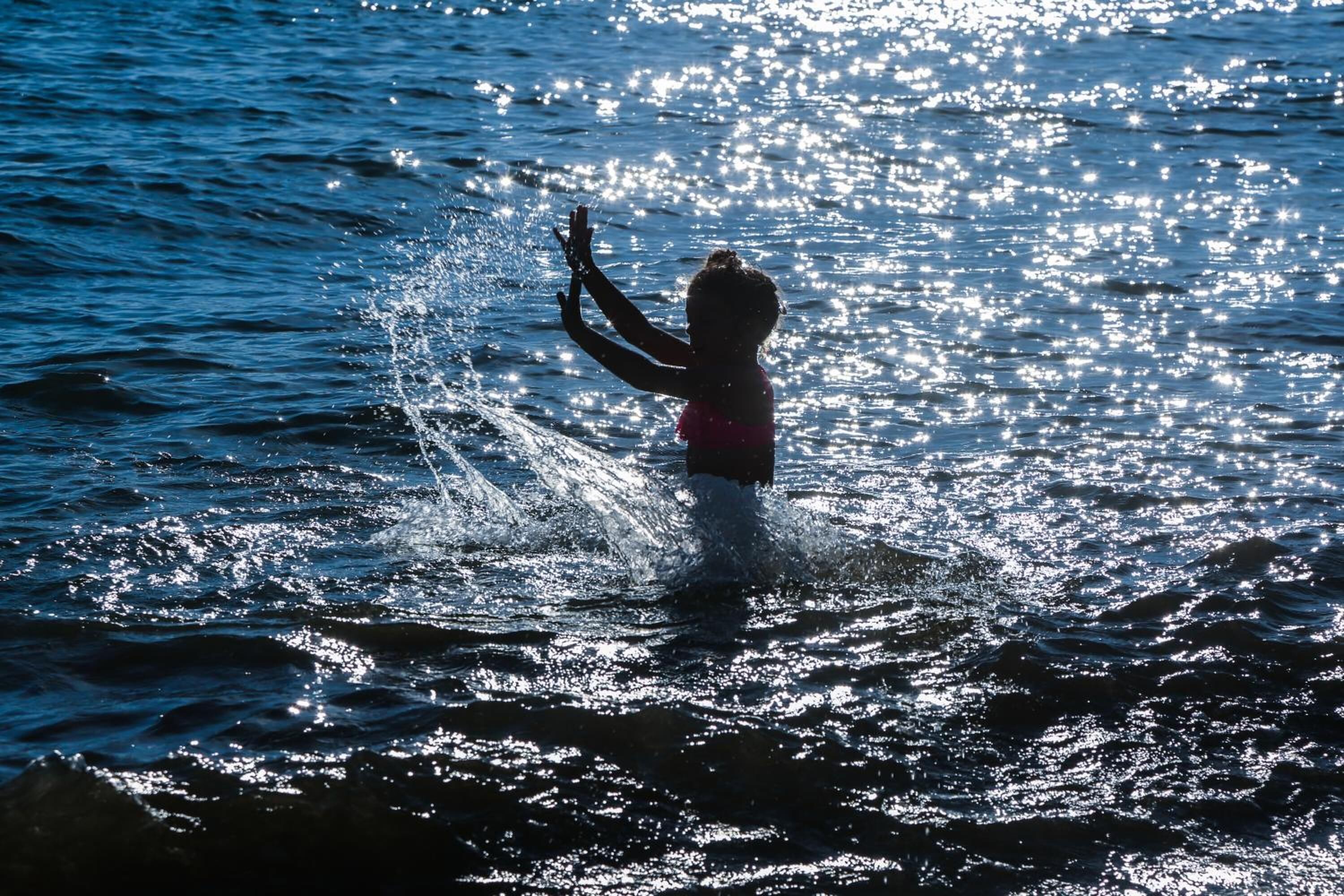 A child playing in the water with sunlight reflecting off the surface.