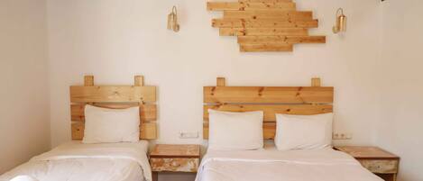 A hotel room with two beds, wooden headboards, white linens, and a wall-mounted wooden art piece.