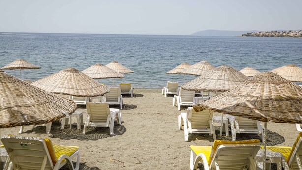 Una spiaggia con file di sdraie bianche e ombrelloni di paglia, che si affaccia su un mare calmo.