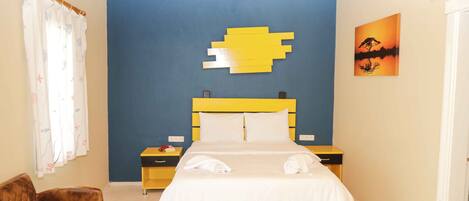 Un dormitorio con cama, mesita de noche, una silla, pared con diseño geométrico amarillo y un cuadro.