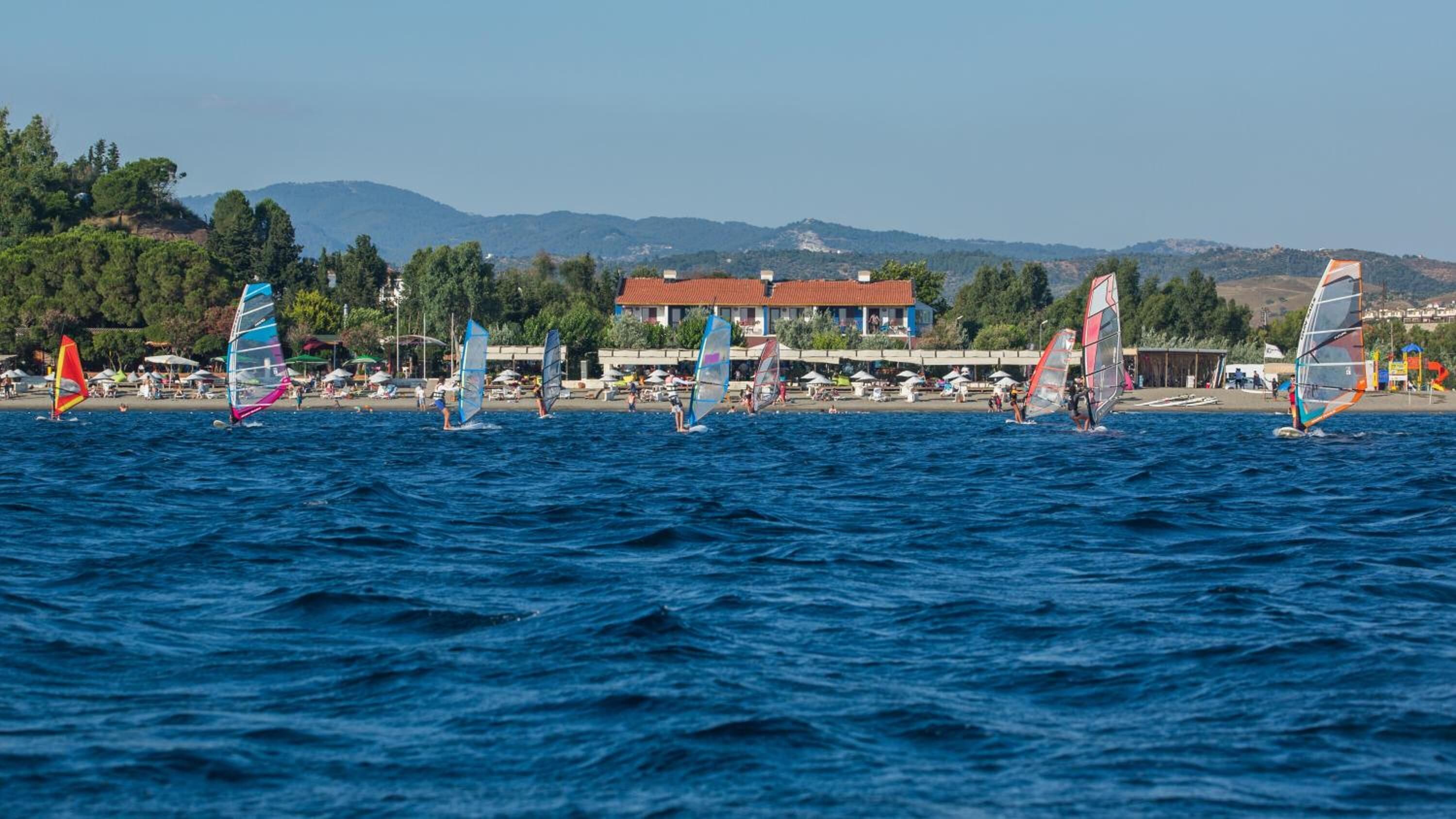 A coastal area with windsurfing activity, a beach, and buildings in the background.