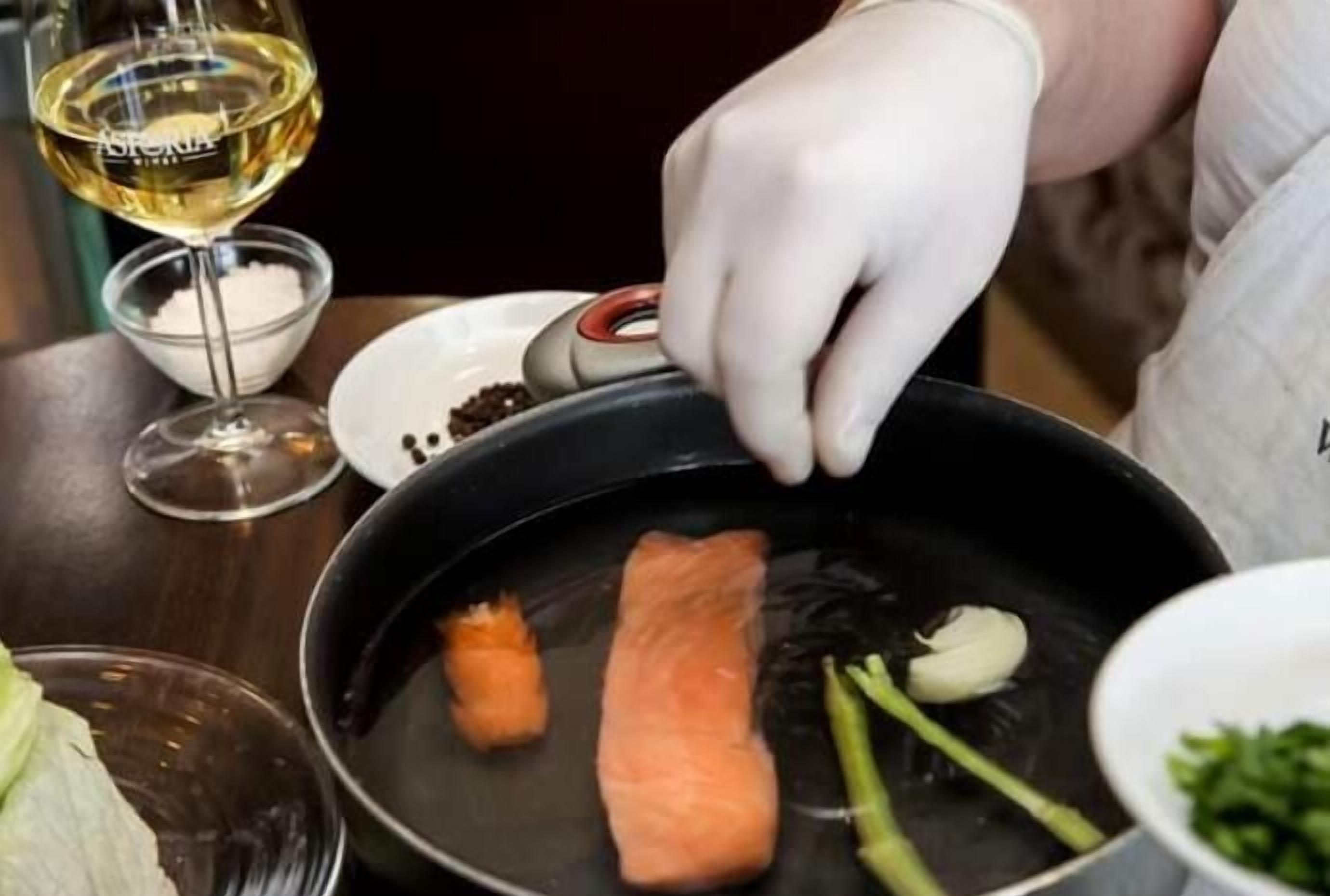 A person cooking salmon with vegetables in a pan.