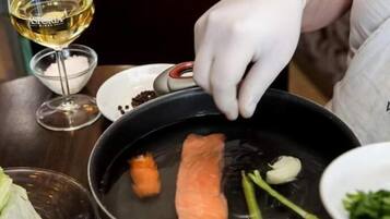 A person cooking salmon with vegetables in a pan.