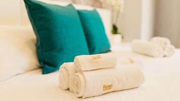 Una cama bien hecha con almohadas blancas y turquesas, y toallas blancas enrolladas con un logotipo.