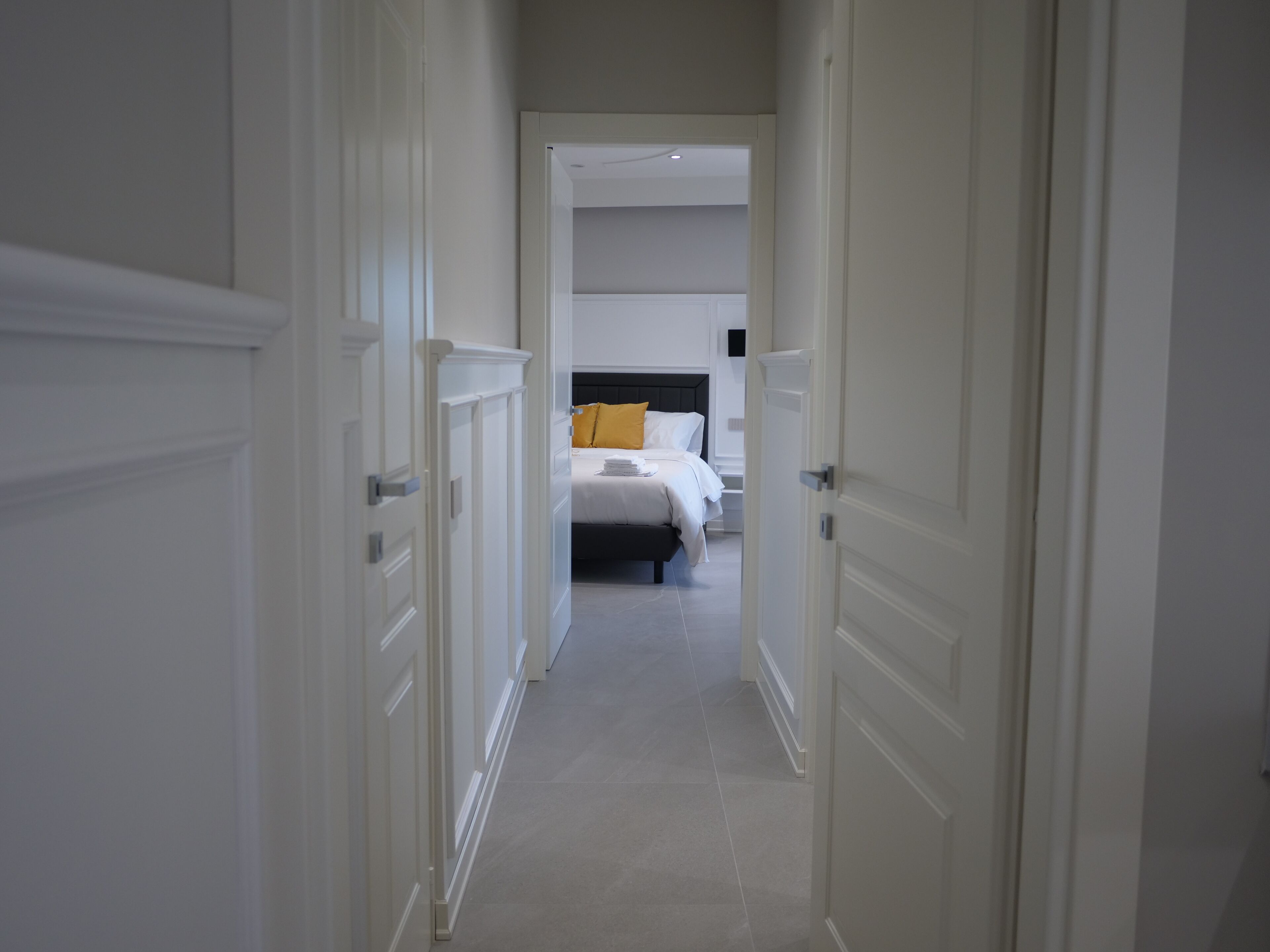 Corredor que leva a um quarto com cama, mesa de cabeceira e criado-mudo.