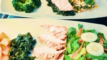Forskellige retter, herunder grillet kylling, broccoli og en salat med salat og agurk.