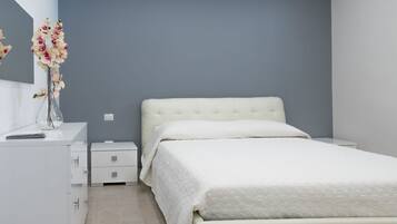 Un dormitorio moderno con una cama grande, una mesita de noche, un aparador y un florero con flores.