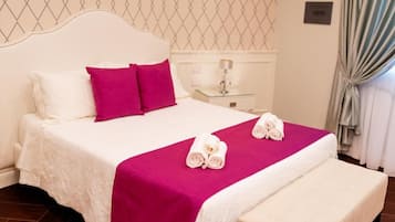 Un lit bien fait, avec une literie blanche et rose, deux serviettes enroulées et un banc au pied du lit.