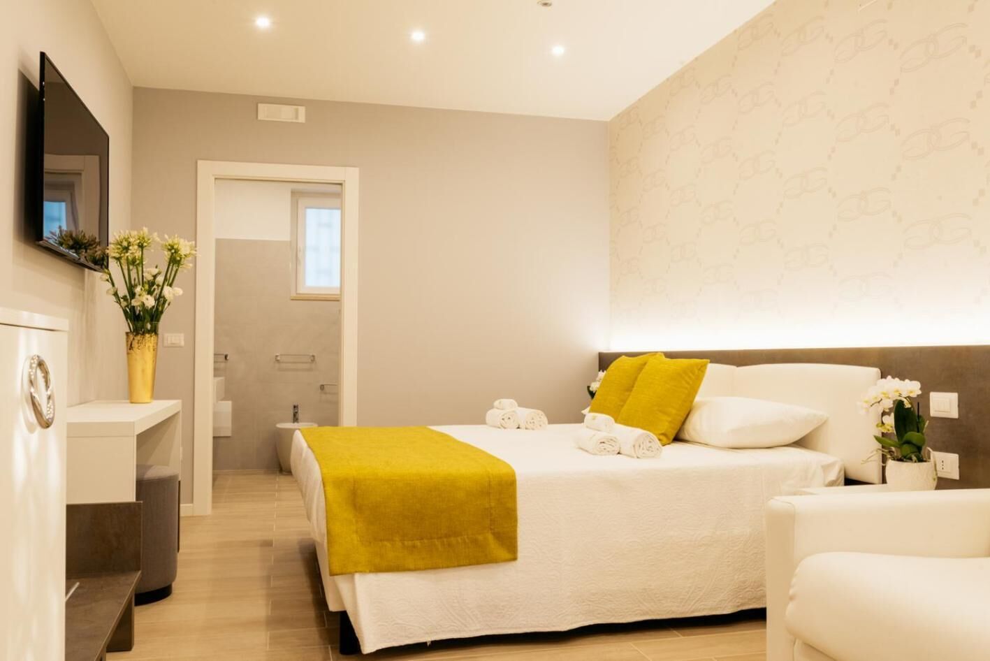 Una habitación de hotel moderna con una cama, una mesita de noche, una silla y un televisor fijado a la pared.