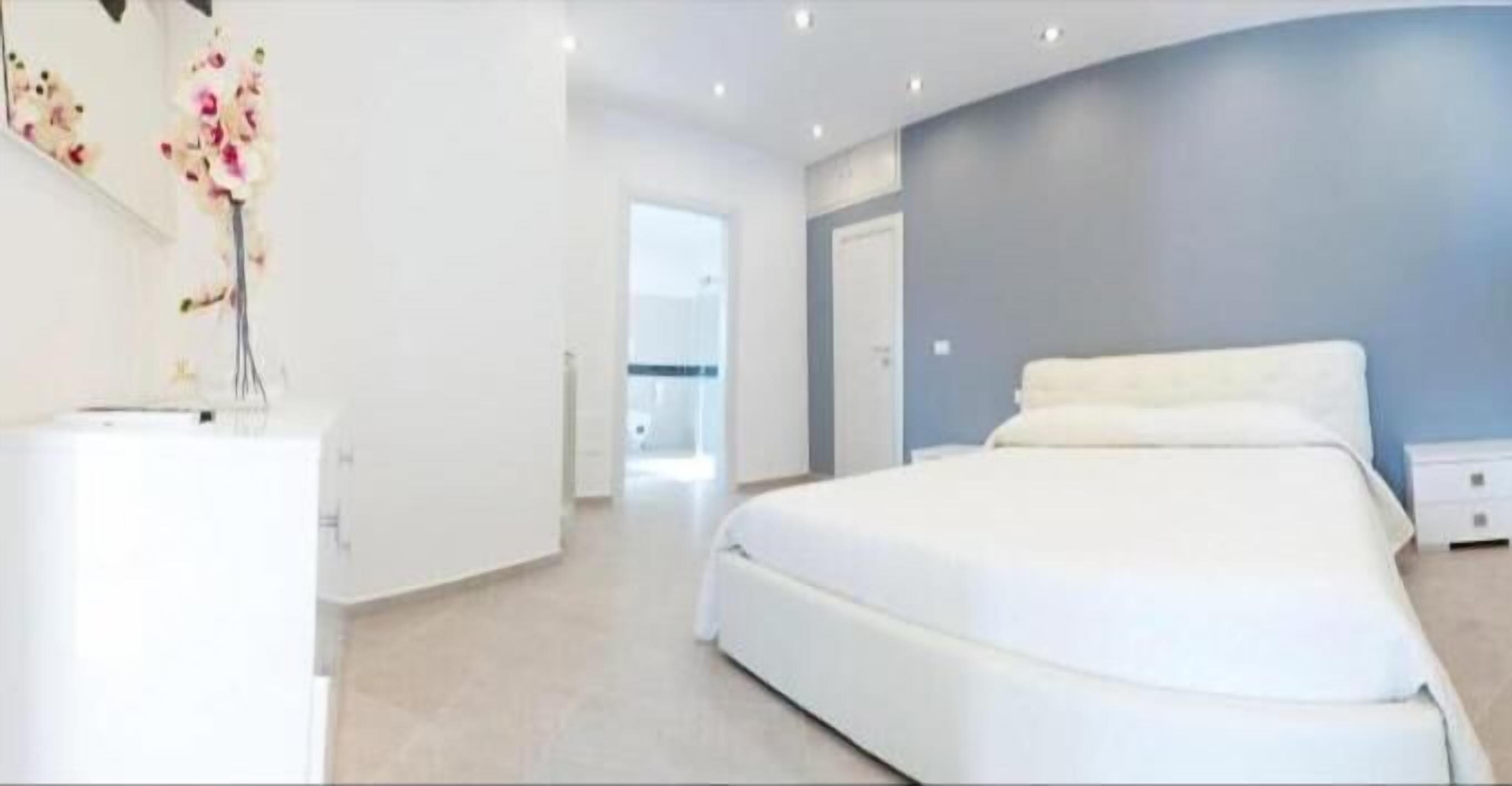 A modern bedroom with a large bed, a nightstand, and a wall-mounted vase with flowers.