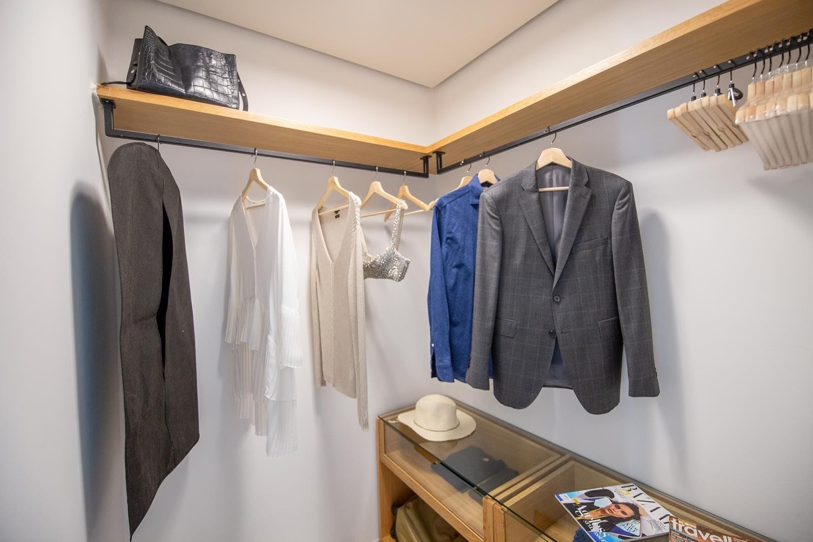 Un dressing avec des vêtements suspendus, une étagère en bois et un magazine sur une table en verre.