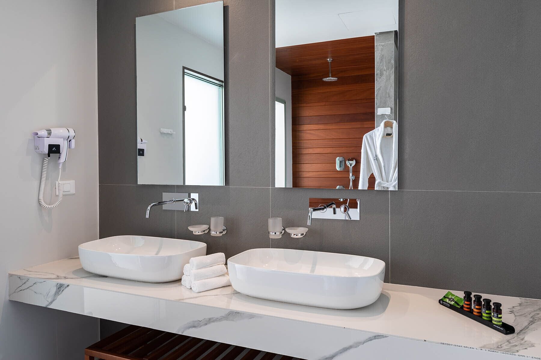 Ein modernes Badezimmer mit zwei großen, weißen Waschbecken, einem Fön, einem Spiegel und einer Wandverkleidung aus Holz.