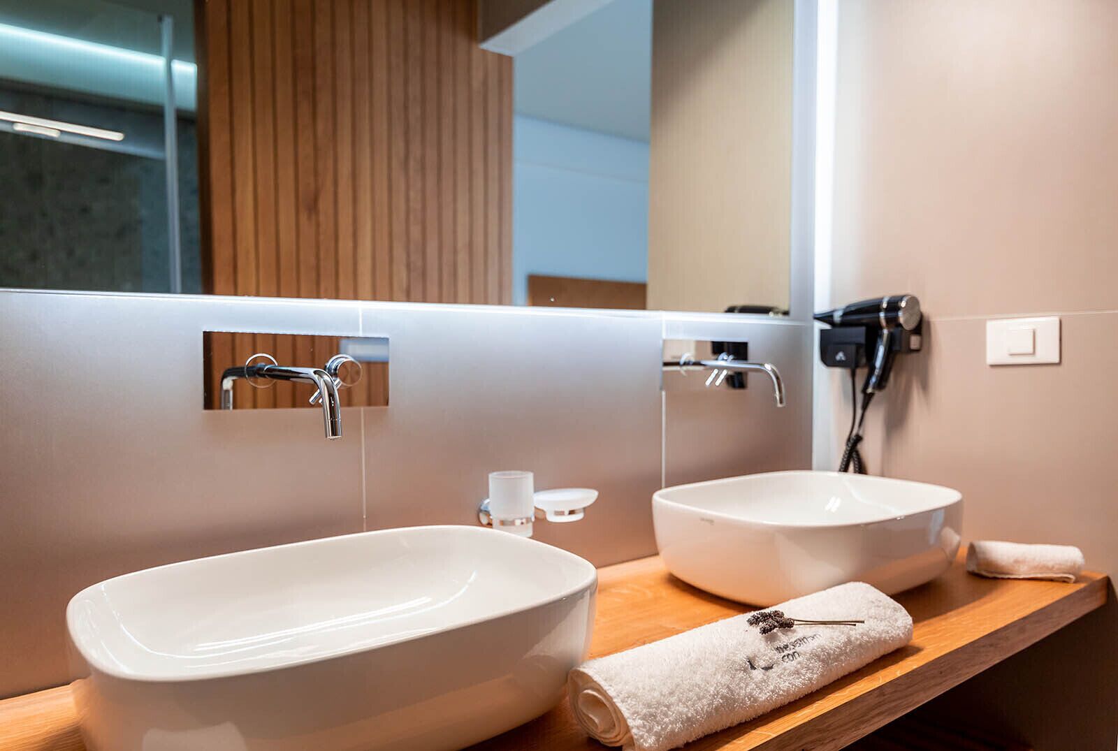 Een moderne badkamer met twee wastafels, een haardroger en een handdoek op het aanrecht.