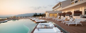 A modern hotel with a pool area, lounge chairs, and a view of the mountains.