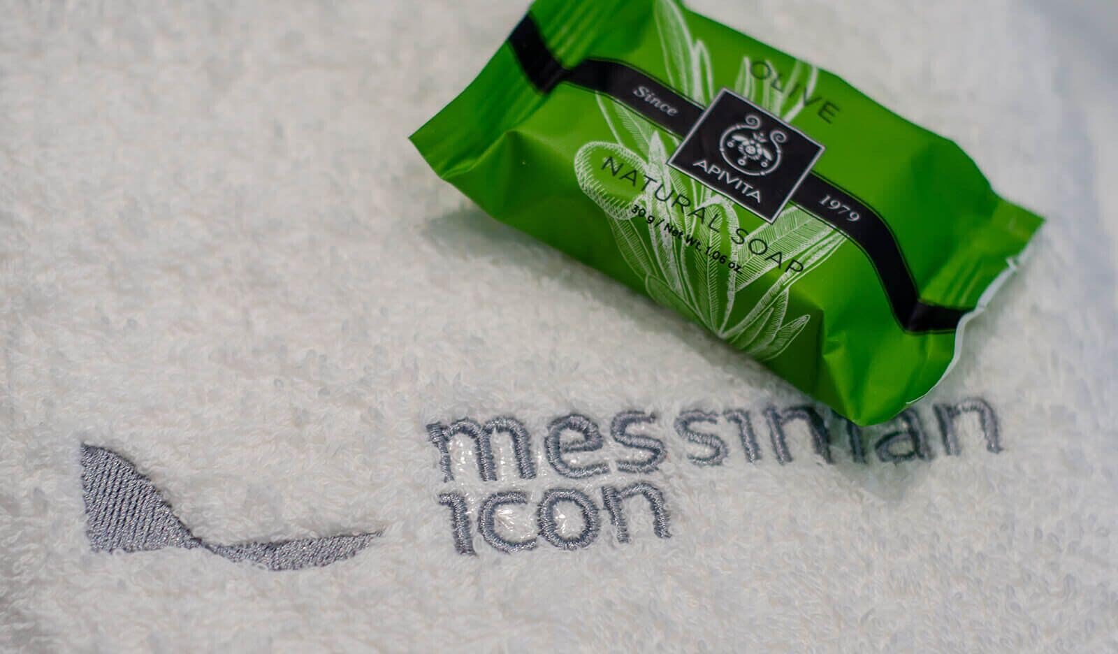 Un paquete verde de jabón natural sobre una toalla blanca con texto bordado.