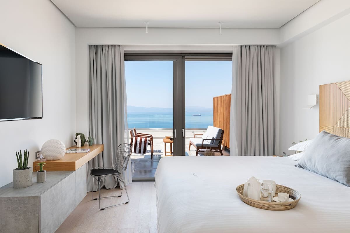 A hotel room with a large bed, a desk with a chair, a TV, and a view of the sea.