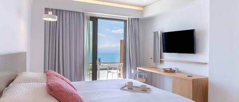 Une chambre d’hôtel moderne dotée d’un grand lit, d’un téléviseur fixé au mur et d’un balcon offrant une vue sur la mer.