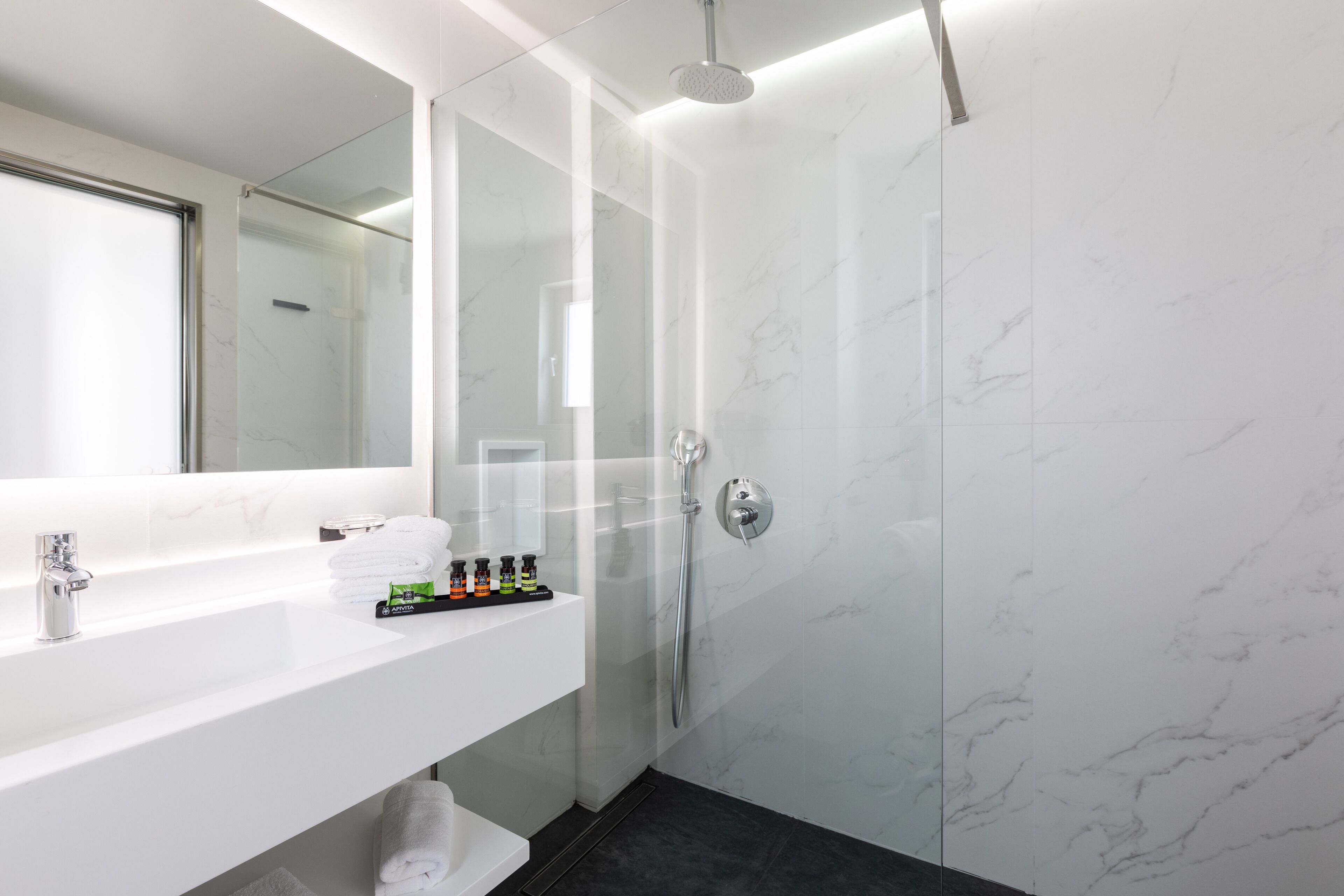 A modern bathroom with a white marble sink, a glass-enclosed shower, and a large mirror.