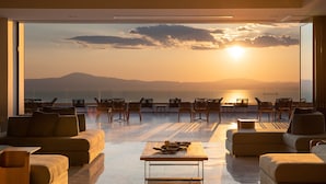 Un vaste espace de vie doté d’une grande fenêtre offrant une vue imprenable sur le coucher de soleil, et aménagé avec des canapés et des tables.