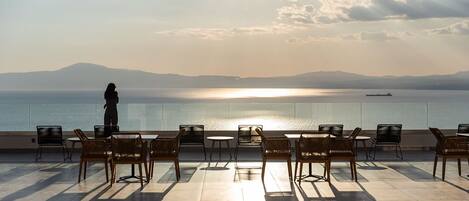 A terrace with chairs and tables overlooking a body of water and distant mountains.