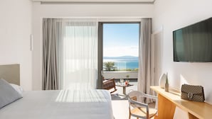 Une chambre d’hôtel comprenant un lit, un bureau, une chaise, une télévision et un balcon avec vue sur la mer.