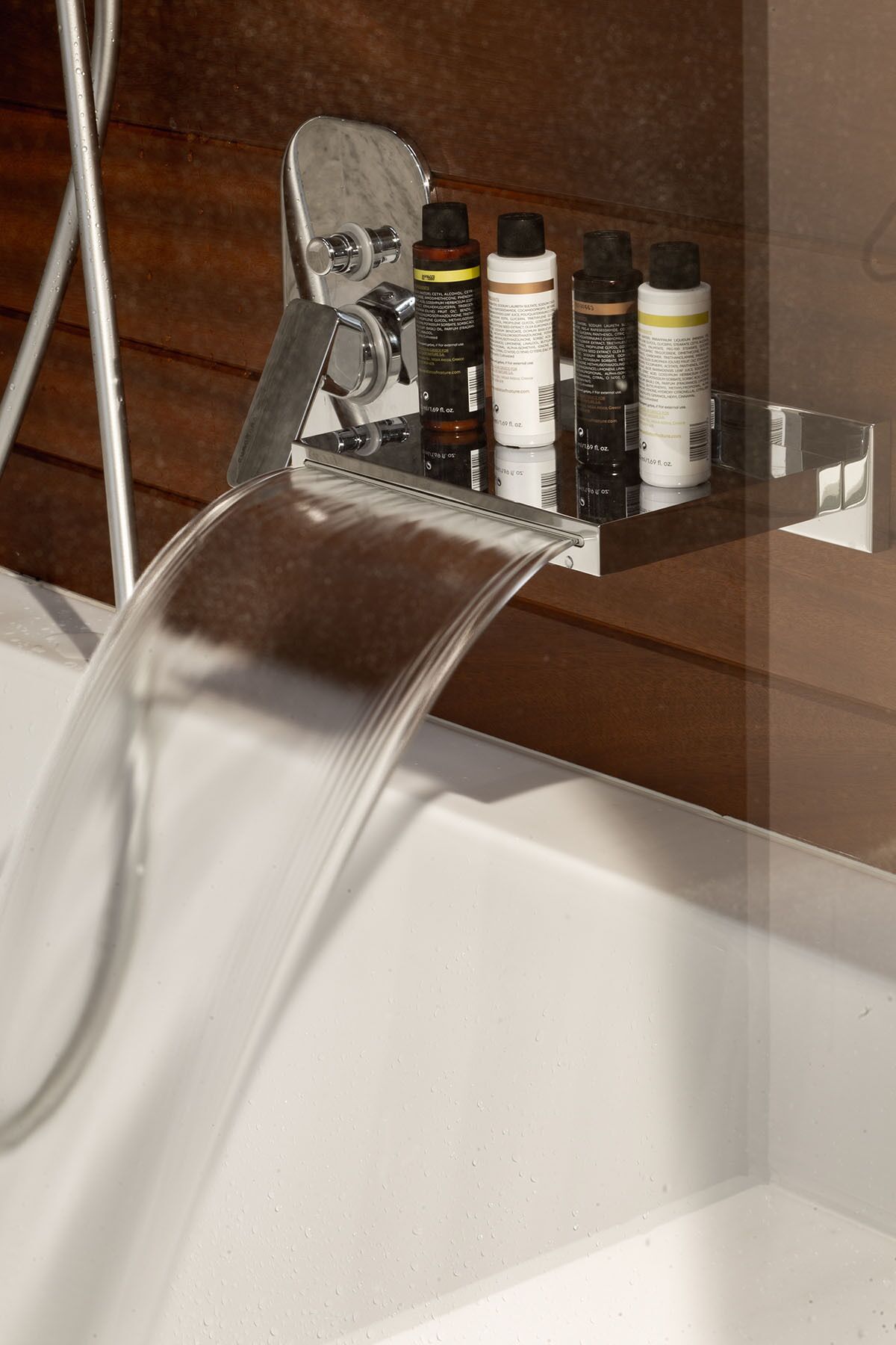 A bathroom with a modern faucet, a showerhead, and a shelf with toiletries.