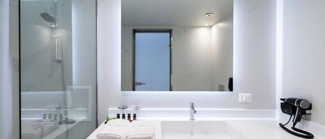 A modern bathroom with a glass-enclosed shower, a white vanity with a large mirror, and a hairdryer mounted on the wall.