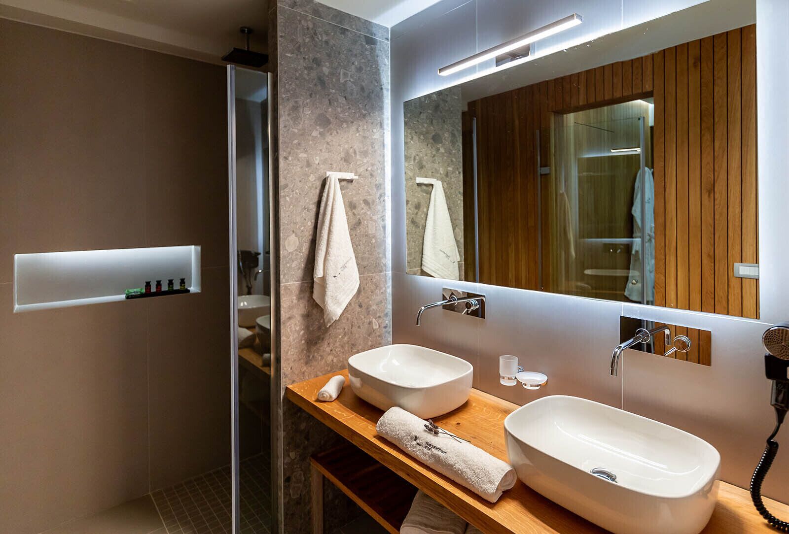 A modern bathroom with two sinks, a large mirror, and a shower.
