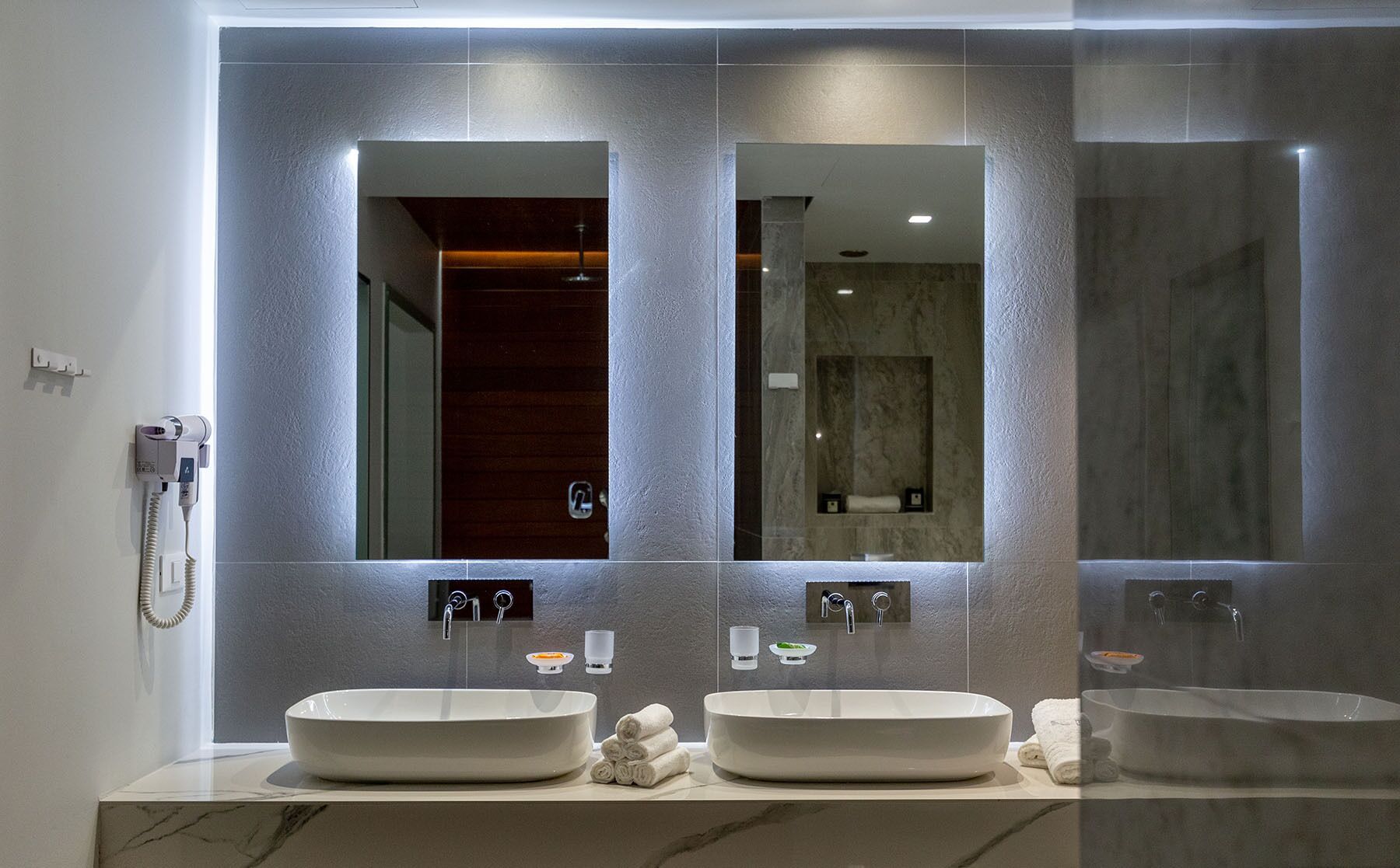 Un baño moderno con dos lavamanos, un secador de pelo y un espejo.