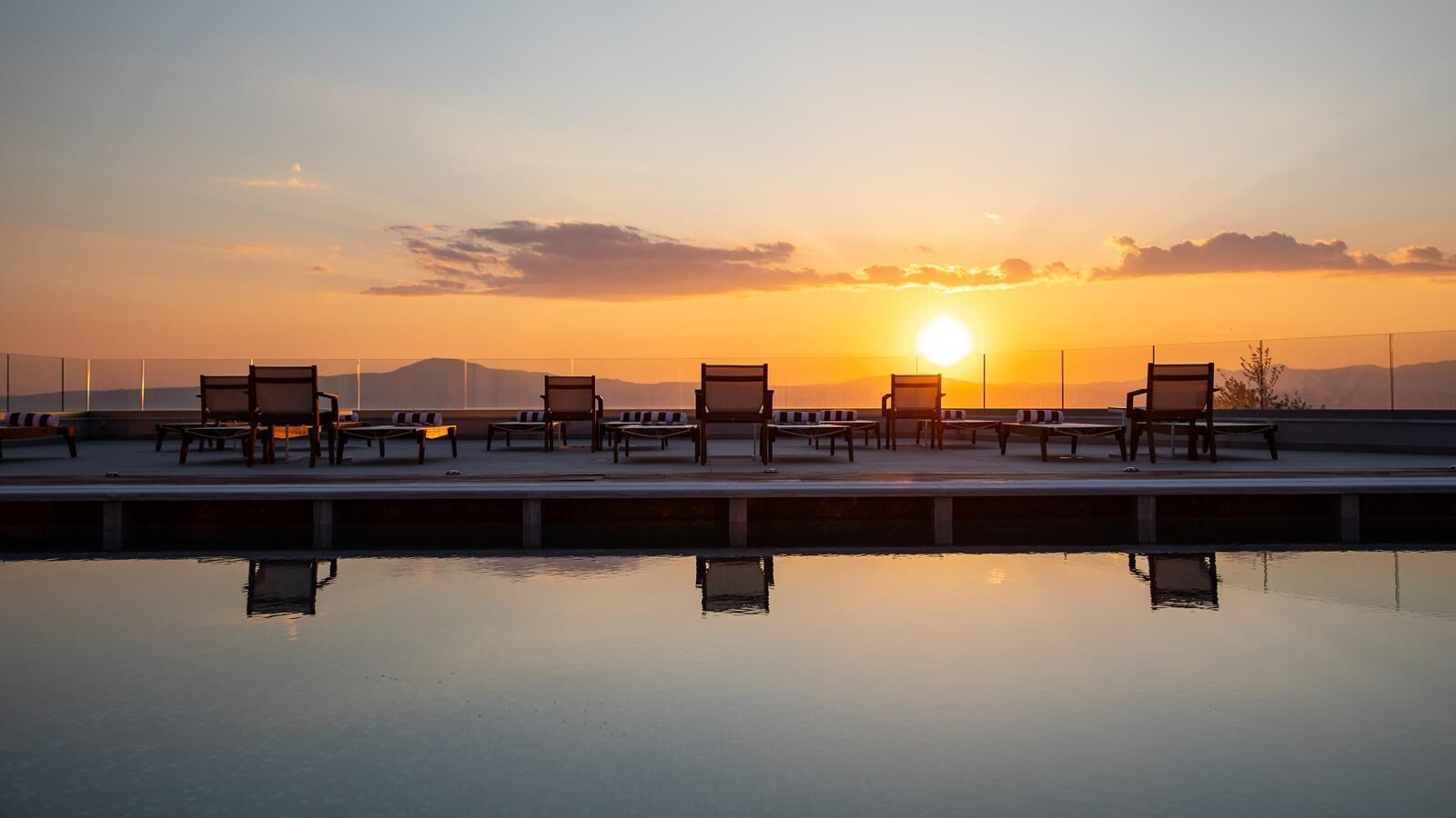 Zona junto a la piscina con sillas de descanso y vista al atardecer.
