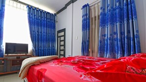 A hotel room with a bed, a television on a wooden stand, and curtains with floral patterns.